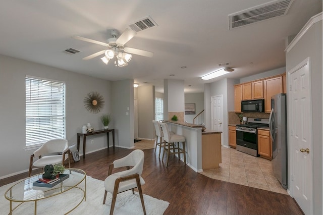 interior space with tasteful backsplash, ceiling fan, a breakfast bar area, light hardwood / wood-style floors, and stainless steel appliances