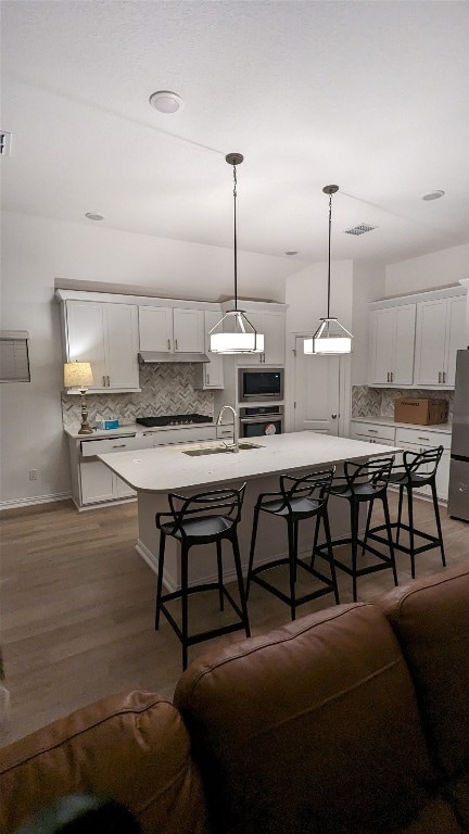 kitchen featuring a center island with sink, a breakfast bar, white cabinetry, stainless steel appliances, and decorative light fixtures