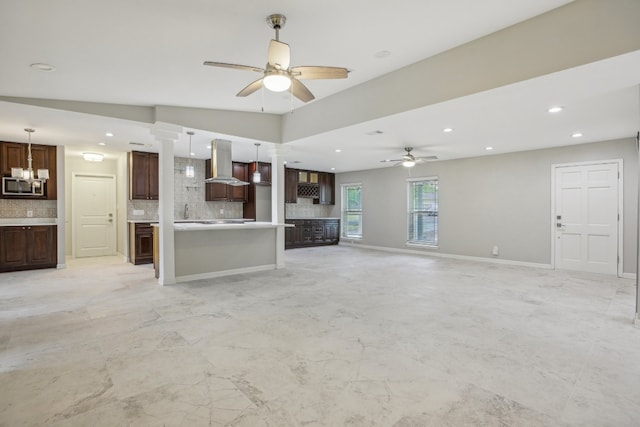 unfurnished living room featuring ceiling fan with notable chandelier, decorative columns, and vaulted ceiling