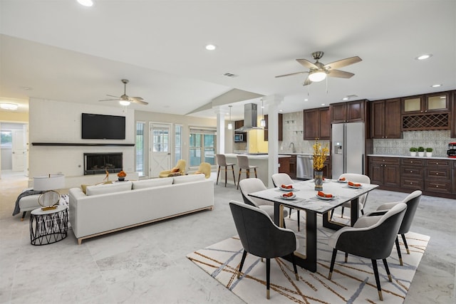 dining space featuring ceiling fan, sink, lofted ceiling, and decorative columns