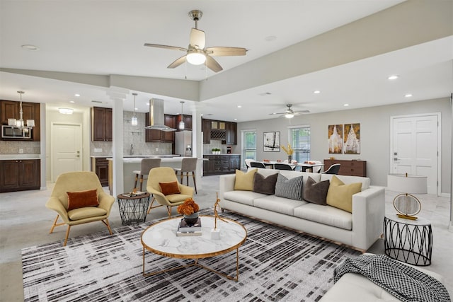 living room featuring ceiling fan with notable chandelier, ornate columns, and lofted ceiling