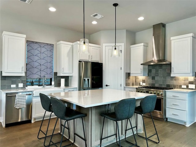 kitchen featuring a breakfast bar, a center island, wall chimney range hood, stainless steel appliances, and white cabinets