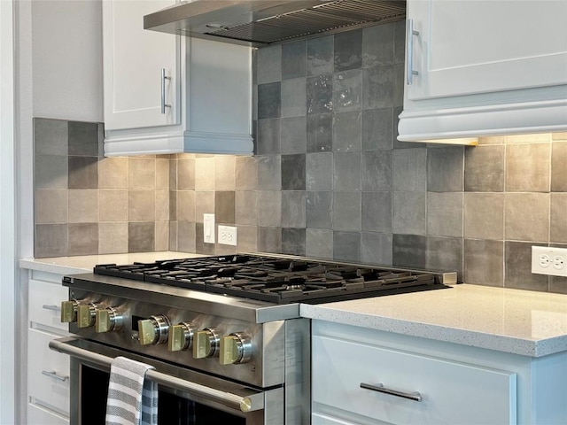 kitchen with high end stainless steel range oven, white cabinetry, backsplash, light stone counters, and wall chimney exhaust hood