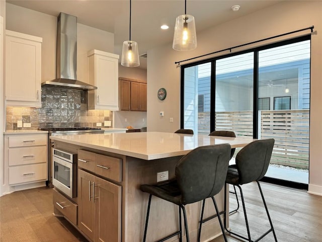 kitchen with wall chimney range hood, white cabinetry, stainless steel microwave, light stone countertops, and a kitchen island