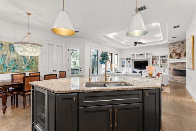 kitchen featuring a center island with sink, sink, decorative light fixtures, a fireplace, and a raised ceiling