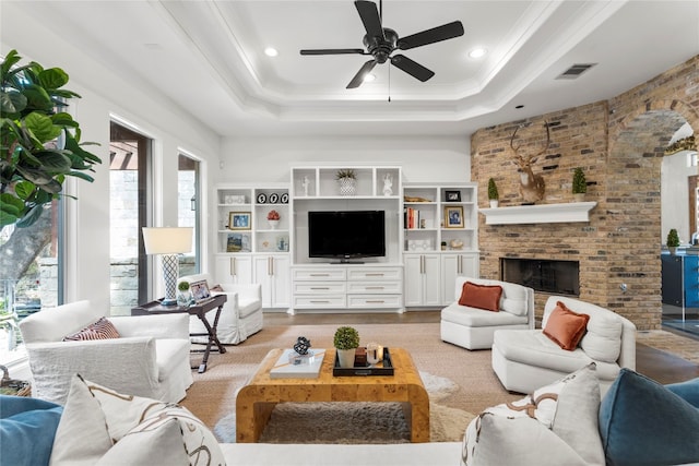 living room with light hardwood / wood-style floors, ornamental molding, ceiling fan, a fireplace, and a raised ceiling