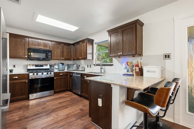 kitchen with sink, light stone counters, dark hardwood / wood-style flooring, kitchen peninsula, and appliances with stainless steel finishes