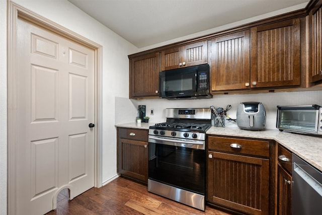 kitchen featuring dark wood-type flooring, decorative backsplash, appliances with stainless steel finishes, dark brown cabinets, and light stone counters