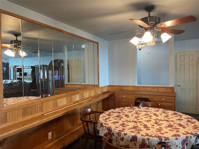 dining space featuring ceiling fan and wooden walls