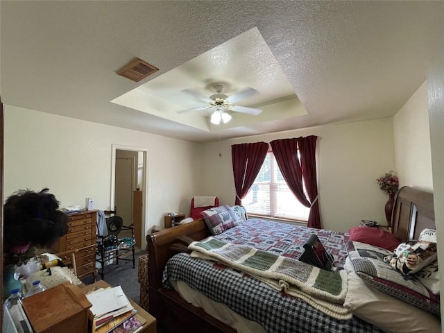 bedroom with a tray ceiling, ceiling fan, dark carpet, and a textured ceiling