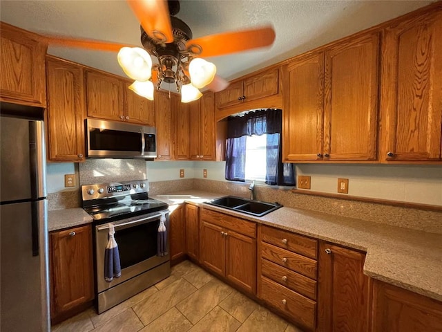 kitchen with light stone countertops, sink, ceiling fan, and stainless steel appliances