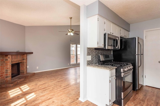 kitchen with appliances with stainless steel finishes, a fireplace, tasteful backsplash, white cabinetry, and light hardwood / wood-style floors