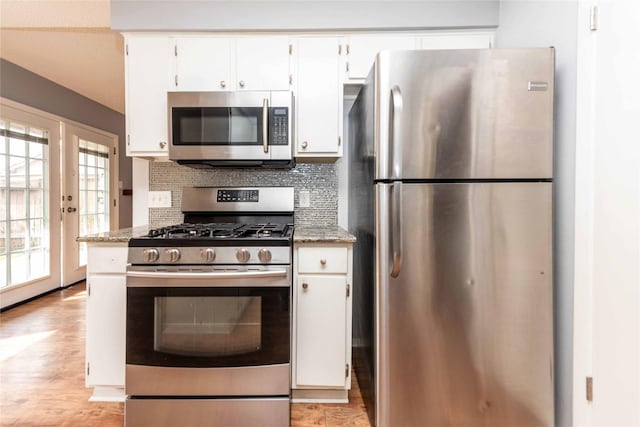 kitchen with stainless steel appliances, light stone counters, tasteful backsplash, white cabinets, and light wood-type flooring