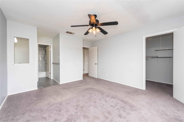 unfurnished bedroom featuring ensuite bathroom, dark colored carpet, a spacious closet, a closet, and ceiling fan