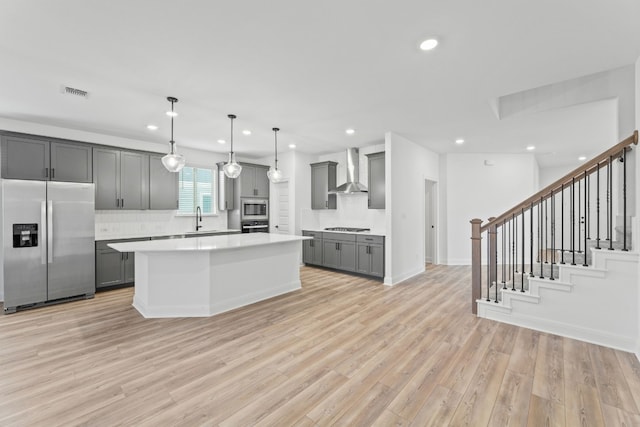 kitchen with a center island, wall chimney range hood, gray cabinets, appliances with stainless steel finishes, and light wood-type flooring