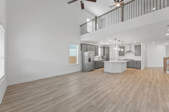 unfurnished living room with ceiling fan, light hardwood / wood-style floors, a towering ceiling, and sink