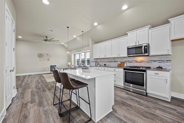 kitchen with wood-type flooring, vaulted ceiling, white cabinets, appliances with stainless steel finishes, and ceiling fan