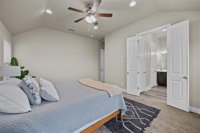 bedroom with light carpet, ensuite bathroom, vaulted ceiling, and ceiling fan