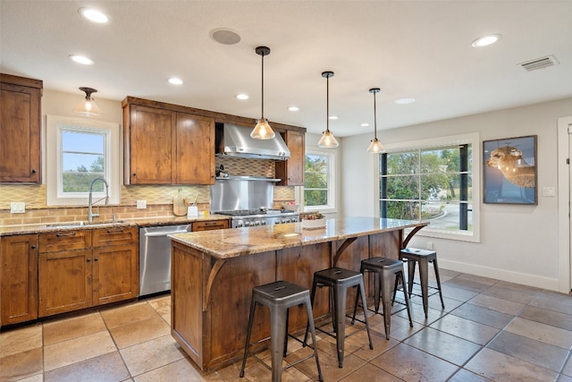 kitchen featuring tasteful backsplash, wall chimney range hood, appliances with stainless steel finishes, hanging light fixtures, and a center island