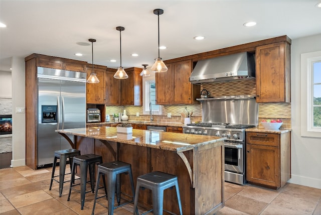 kitchen with light stone counters, a center island, premium appliances, pendant lighting, and wall chimney range hood