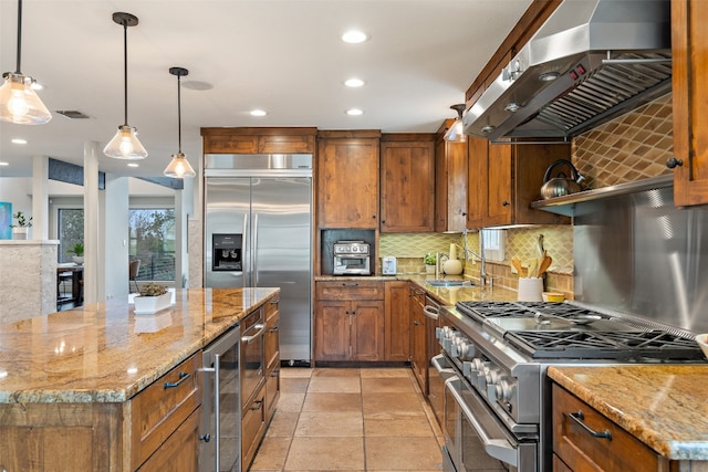 kitchen featuring premium appliances, a center island, hanging light fixtures, wall chimney range hood, and light stone countertops