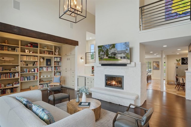 living area with a glass covered fireplace, a notable chandelier, wood finished floors, and a towering ceiling