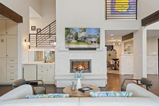 living area with stairway, a fireplace, dark wood-type flooring, and a towering ceiling