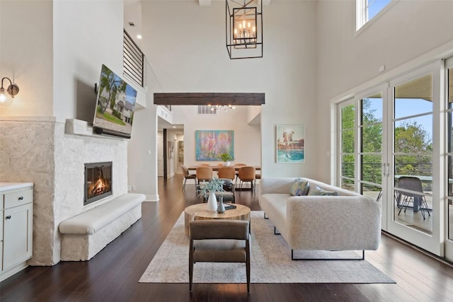living area featuring visible vents, wood-type flooring, a chandelier, a glass covered fireplace, and a high ceiling