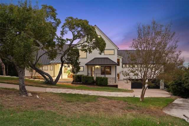 view of front facade featuring a standing seam roof, a yard, driveway, and metal roof