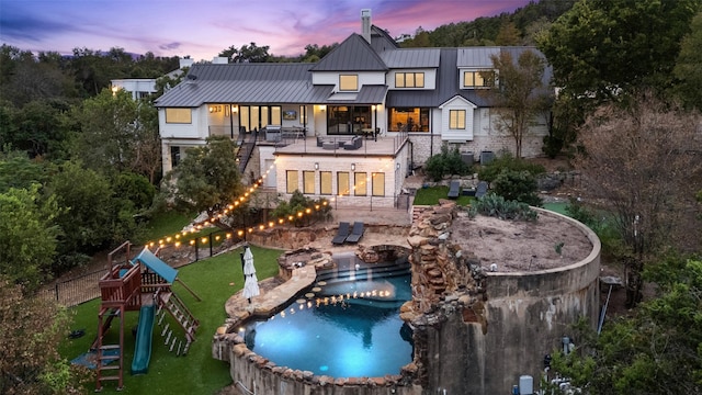 back house at dusk featuring a balcony, a playground, and a patio