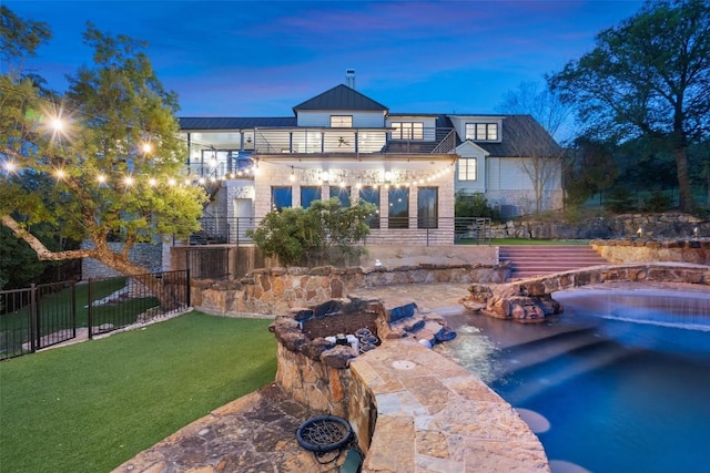 back of house at dusk with a yard, fence, and a balcony