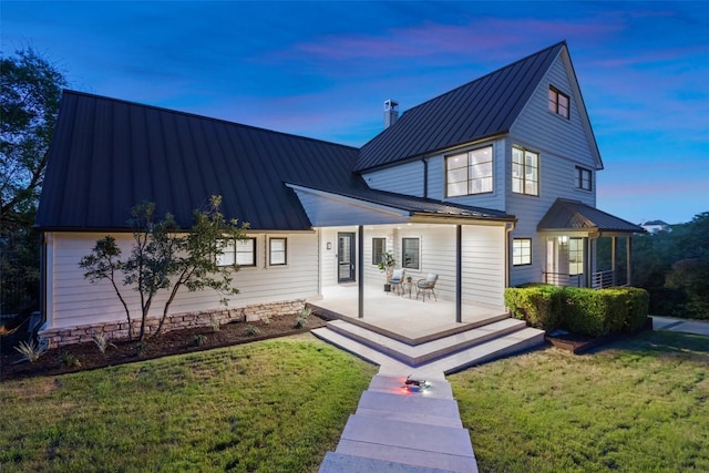 back of property at dusk featuring a standing seam roof, a patio, a yard, and metal roof