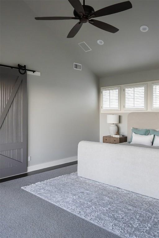 carpeted bedroom with a ceiling fan, vaulted ceiling, a barn door, and visible vents