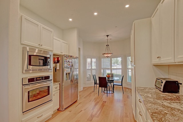 kitchen with light wood-type flooring, white cabinets, light stone counters, and stainless steel appliances