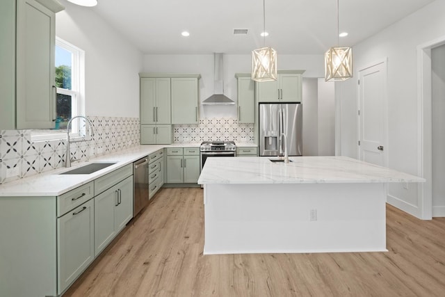 kitchen featuring wall chimney range hood, sink, a center island, appliances with stainless steel finishes, and light stone counters