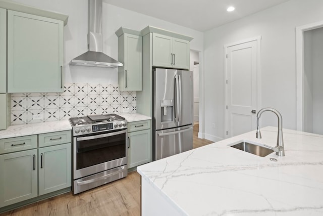 kitchen with light stone counters, appliances with stainless steel finishes, wall chimney range hood, and light hardwood / wood-style floors