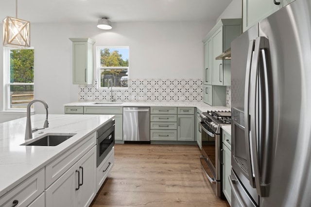 kitchen featuring decorative light fixtures, stainless steel appliances, sink, and light wood-type flooring