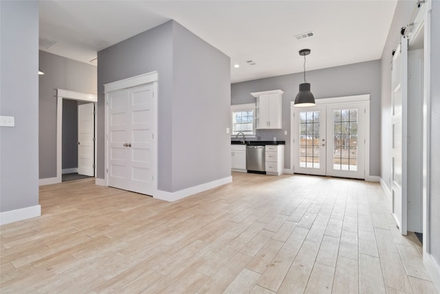 unfurnished living room with french doors, sink, light hardwood / wood-style flooring, and a barn door