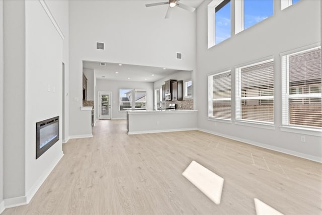 unfurnished living room featuring light hardwood / wood-style floors, ceiling fan, a high ceiling, and a wealth of natural light