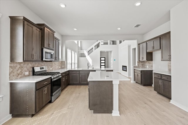 kitchen with a kitchen island, kitchen peninsula, stainless steel appliances, dark brown cabinetry, and light hardwood / wood-style flooring