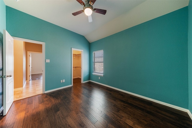 unfurnished bedroom with a spacious closet, dark wood-type flooring, vaulted ceiling, and ceiling fan