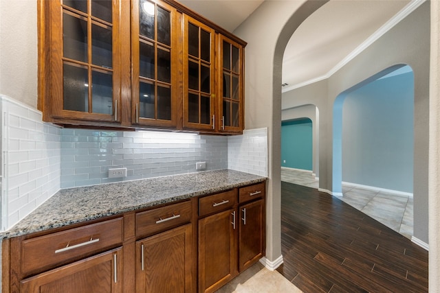 kitchen featuring light stone counters, crown molding, dark hardwood / wood-style flooring, and backsplash