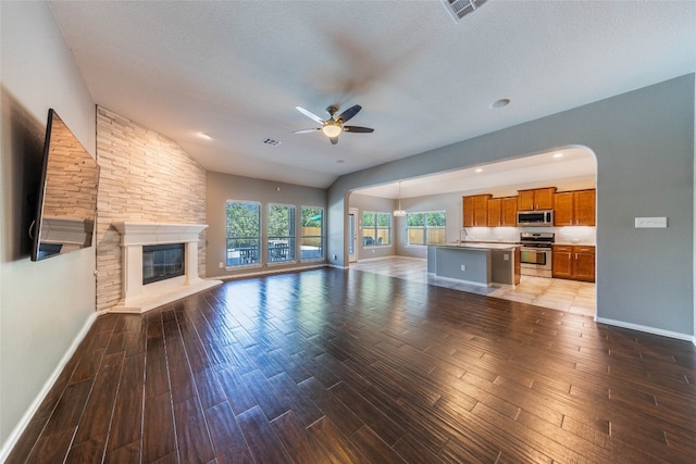 unfurnished living room with sink, a stone fireplace, a textured ceiling, ceiling fan, and dark hardwood / wood-style floors