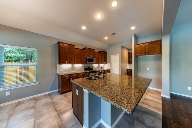 kitchen with sink, stainless steel appliances, dark stone counters, a breakfast bar, and a kitchen island with sink