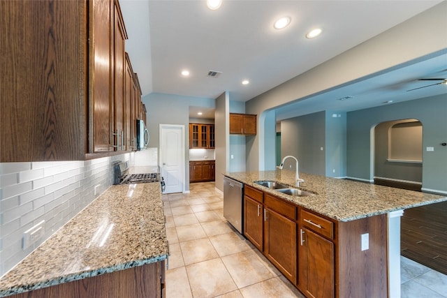 kitchen with an island with sink, sink, light stone countertops, appliances with stainless steel finishes, and tasteful backsplash