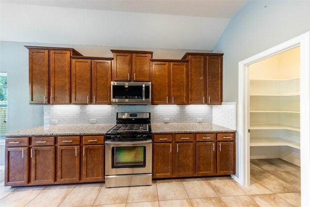 kitchen featuring light stone countertops, vaulted ceiling, appliances with stainless steel finishes, and tasteful backsplash