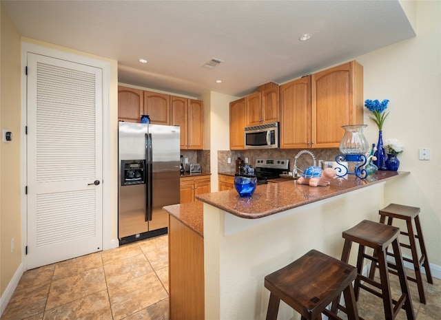 kitchen with backsplash, appliances with stainless steel finishes, a breakfast bar area, and kitchen peninsula