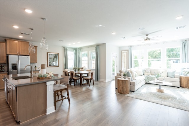 kitchen with an island with sink, sink, stainless steel fridge with ice dispenser, decorative light fixtures, and dark hardwood / wood-style flooring