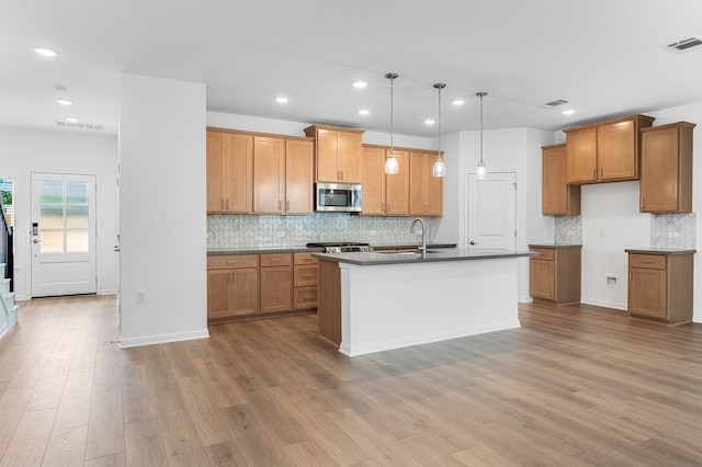 kitchen with brown cabinetry, visible vents, tasteful backsplash, a sink, and stainless steel microwave