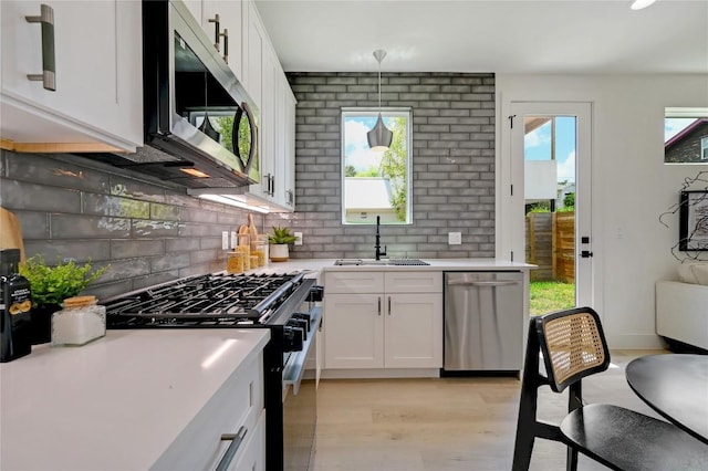 kitchen featuring white cabinets, sink, stainless steel appliances, and hanging light fixtures